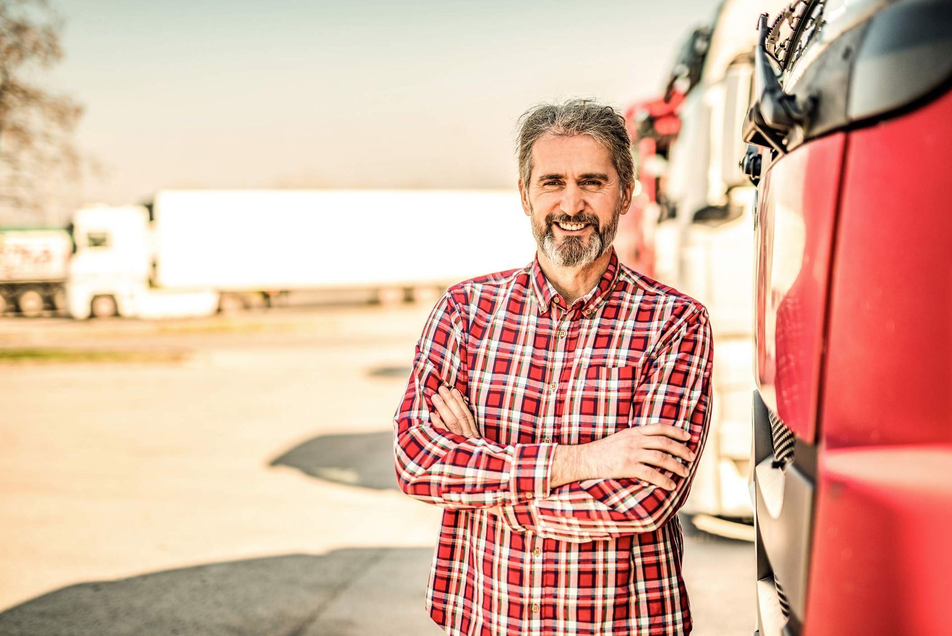 A man in a plaid shirt is standing in front of a truck with his arms crossed.