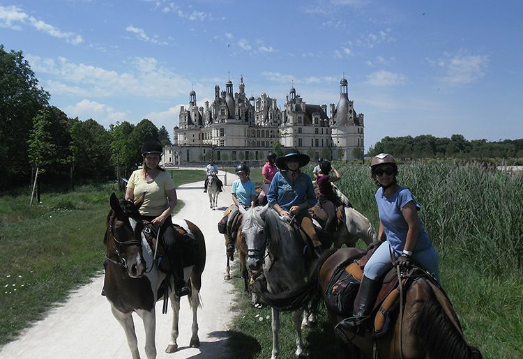 People riding horses on a trail with a large castle in the background