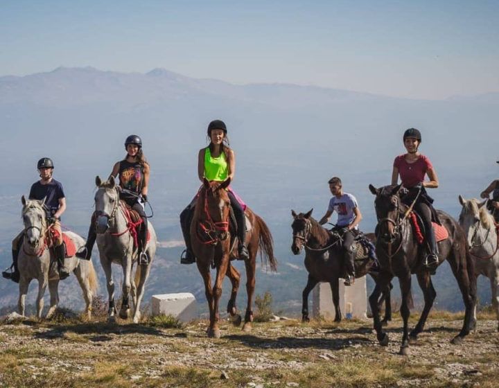 Group of horseback riders on a hilltop with mountains in the background
