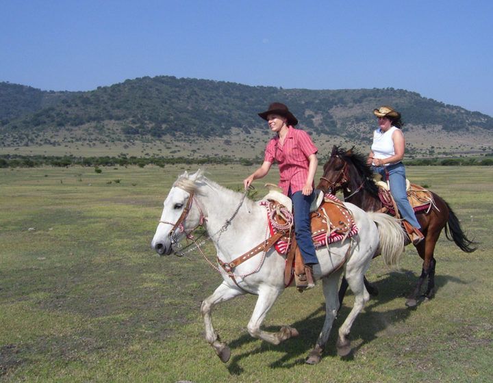 Two riders on horses in a grassy field with hills in the background