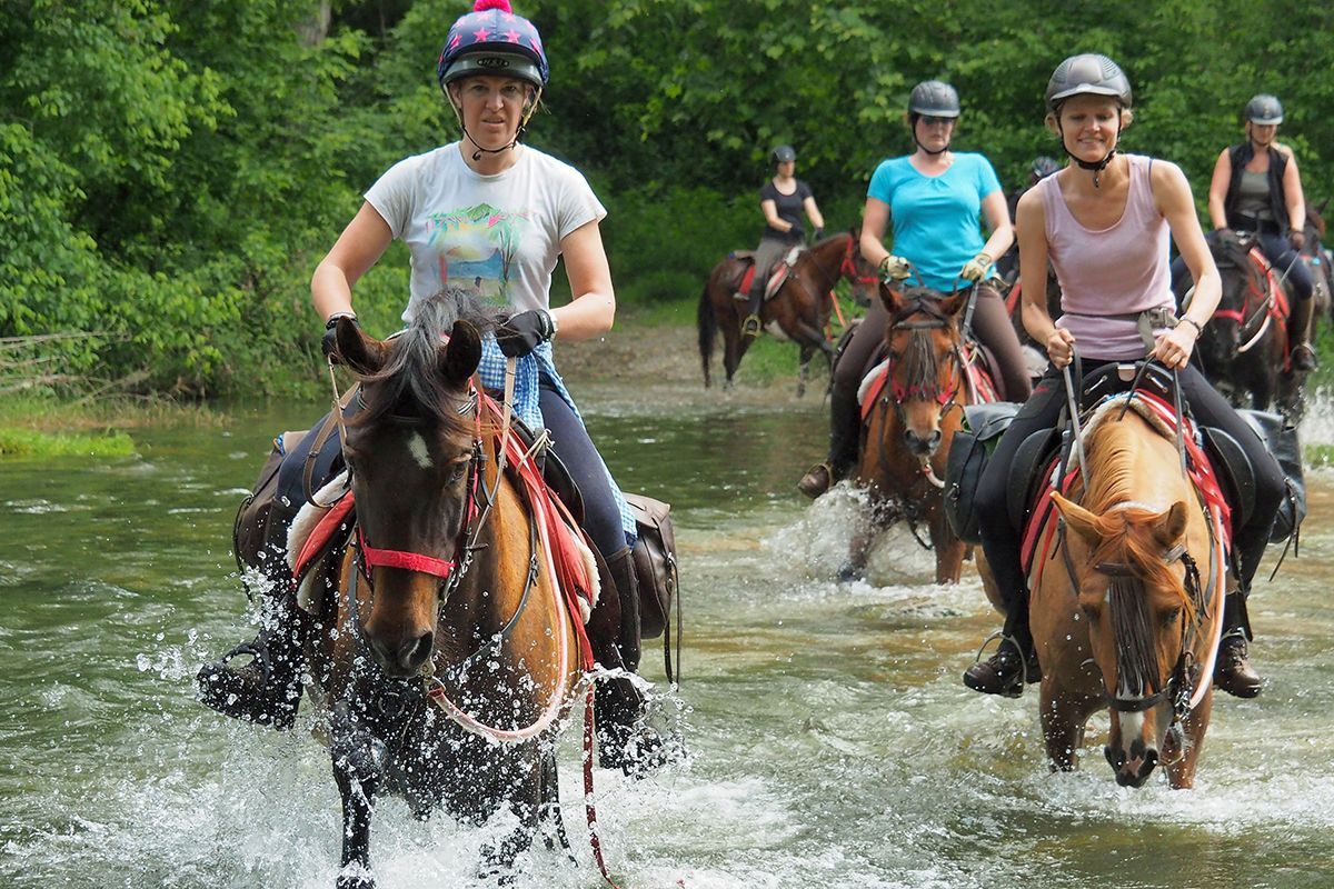 Group horseback riding on a narrow stone bridge over a lush green gorge