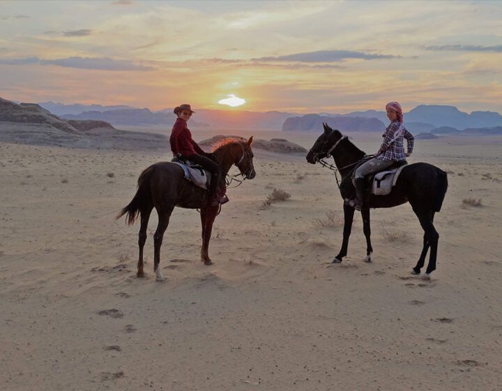 Two riders on horses at sunset in a sandy desert landscape