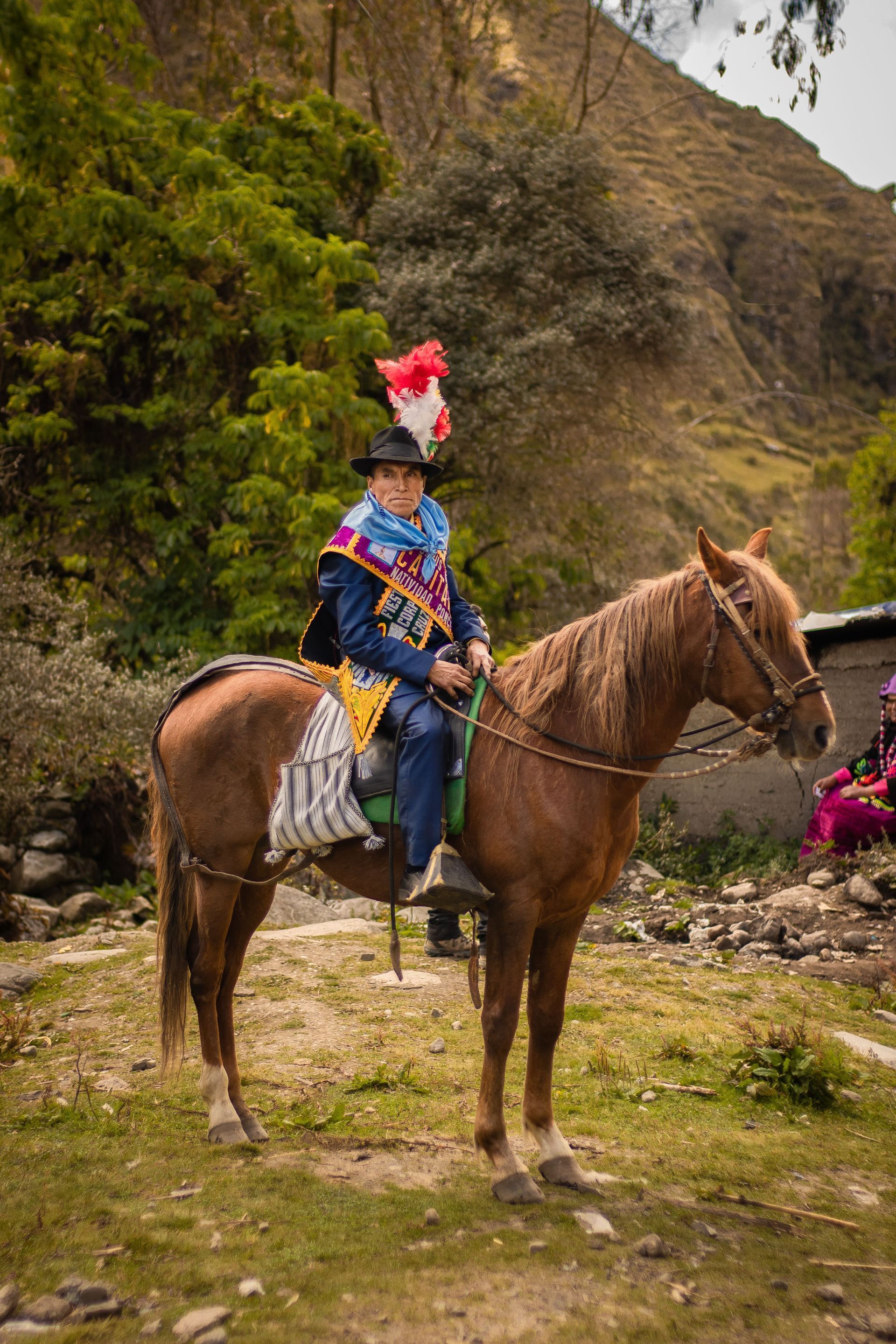 Person in colorful traditional clothing rides a brown horse on a mountain path