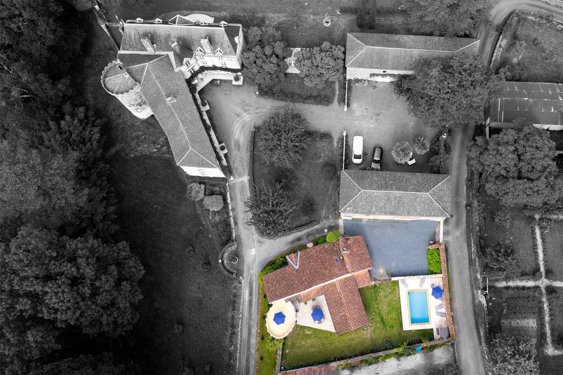 Aerial view of a building with an orange roof and green yard surrounded by black and white buildings and trees.