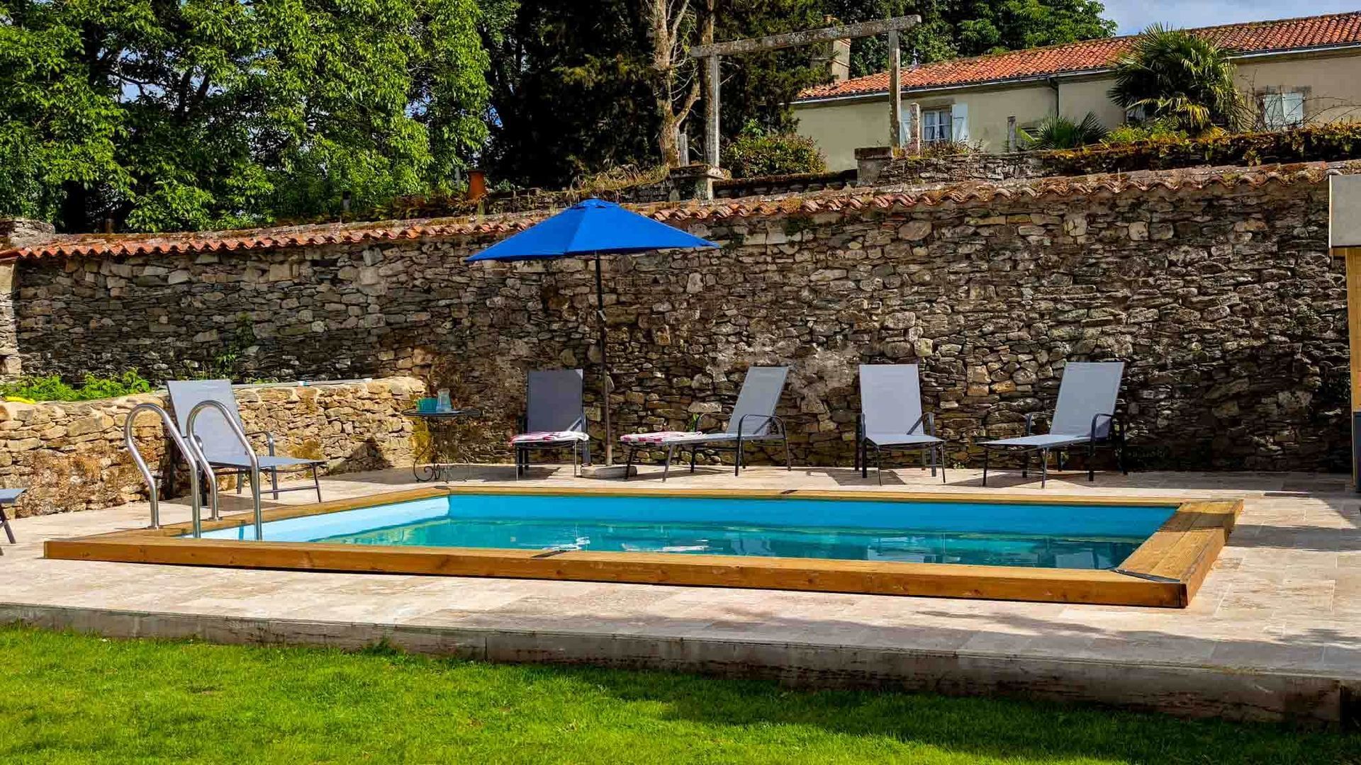 Backyard pool with lounge chairs, blue umbrella, and stone wall in the background
