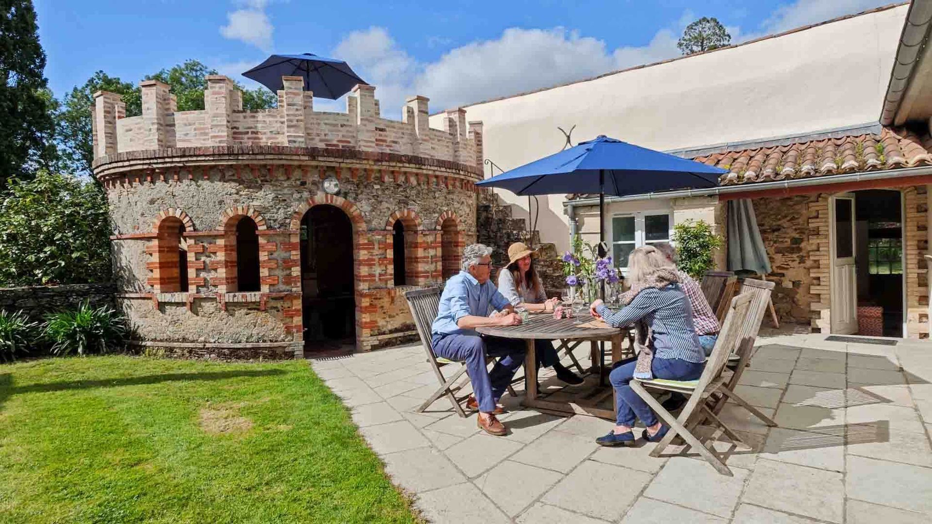People dining outdoors at a table beside a brick patio building under a blue umbrella