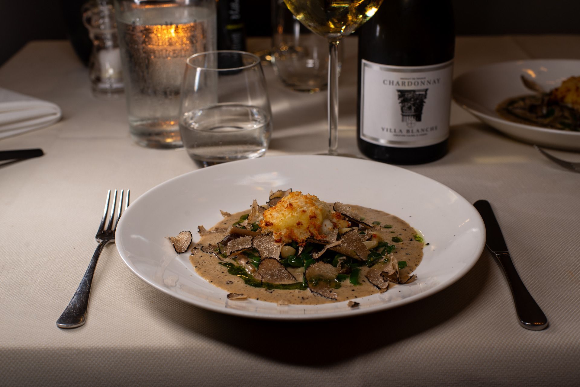 Bord met gastronomische gerechten met truffels, een gefrituurde bal en een fles wijn.