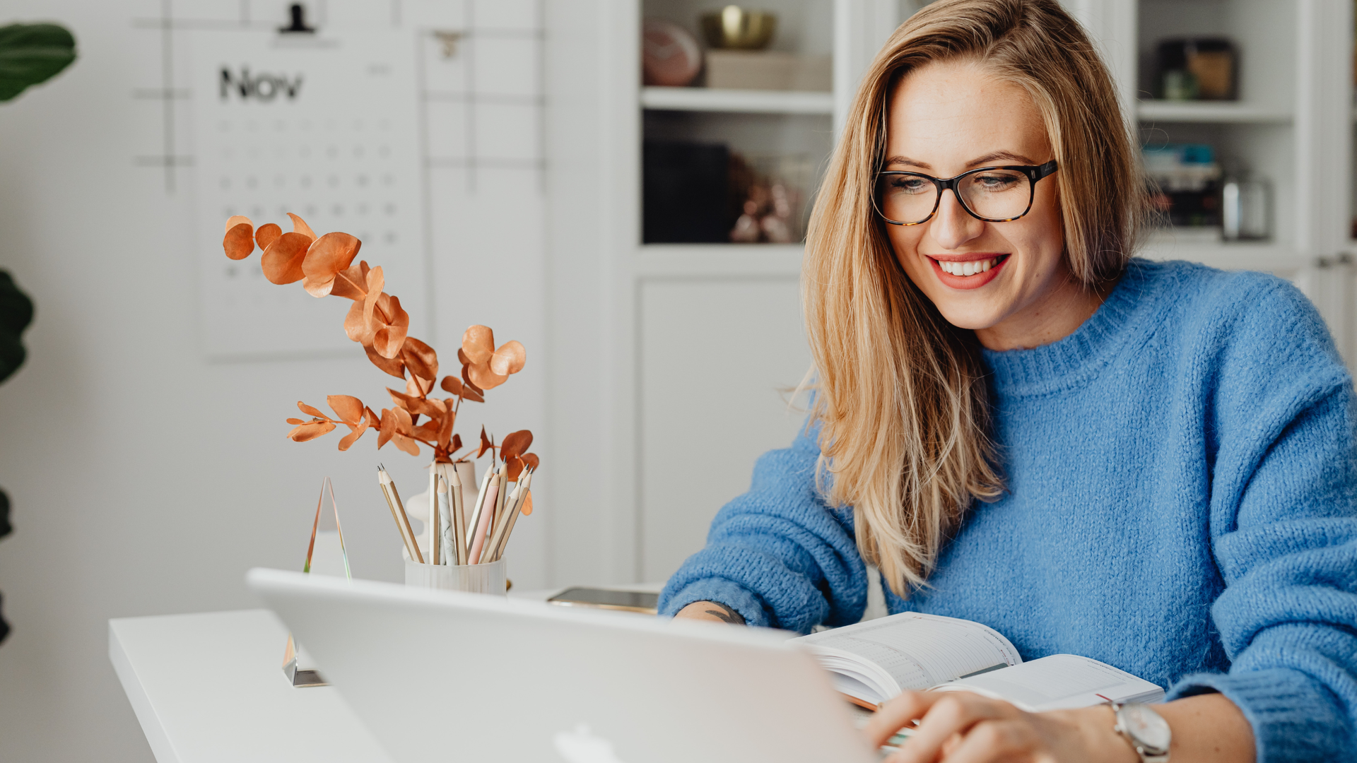 Woman sitting at a desk, smiling as she works on a laptop