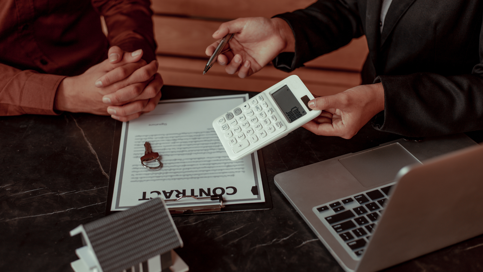 Two people reviewing a rental agreement, one holding a calculator, with a model house on the table
