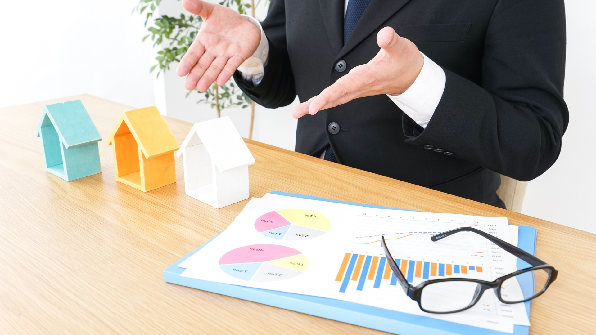 Man gesturing at a table covered with printed graphs, glasses, and model houses