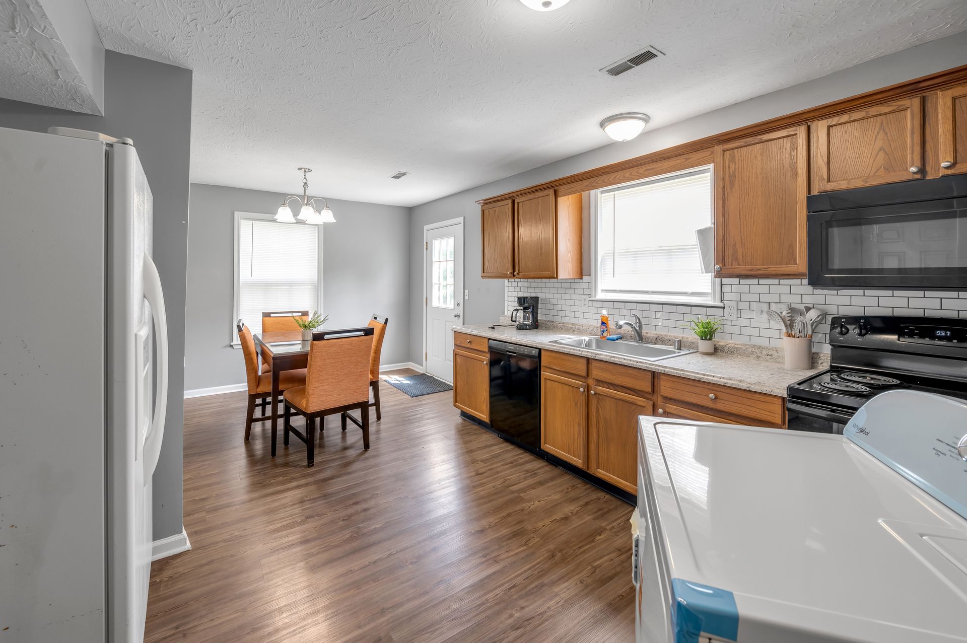 Eat-in kitchen with oak cabinets, subway tile backsplash, black appliances, and a table for four.