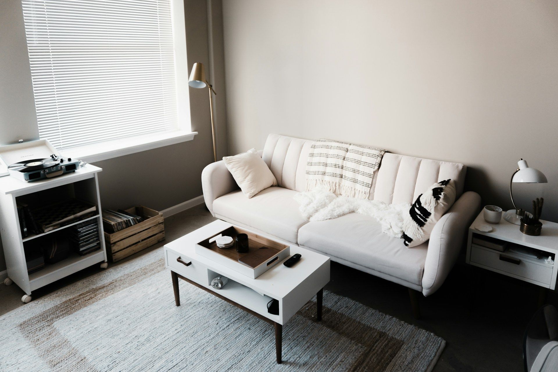 Cozy living room with a white couch, rug, coffee table, and side tables. A record player sits near a window.