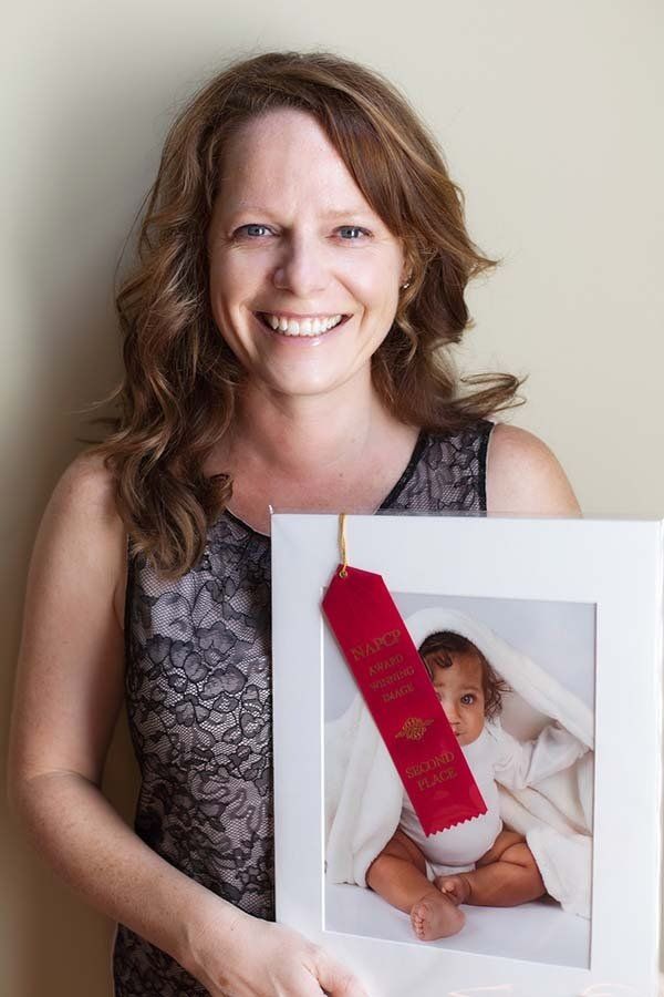 Woman holding a framed baby photo with a red ribbon badge attached