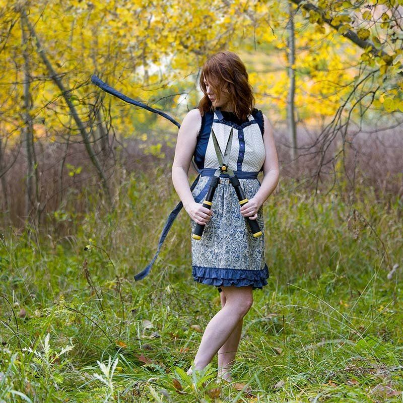 Woman in a patterned dress standing in a grassy field with yellow autumn trees behind her