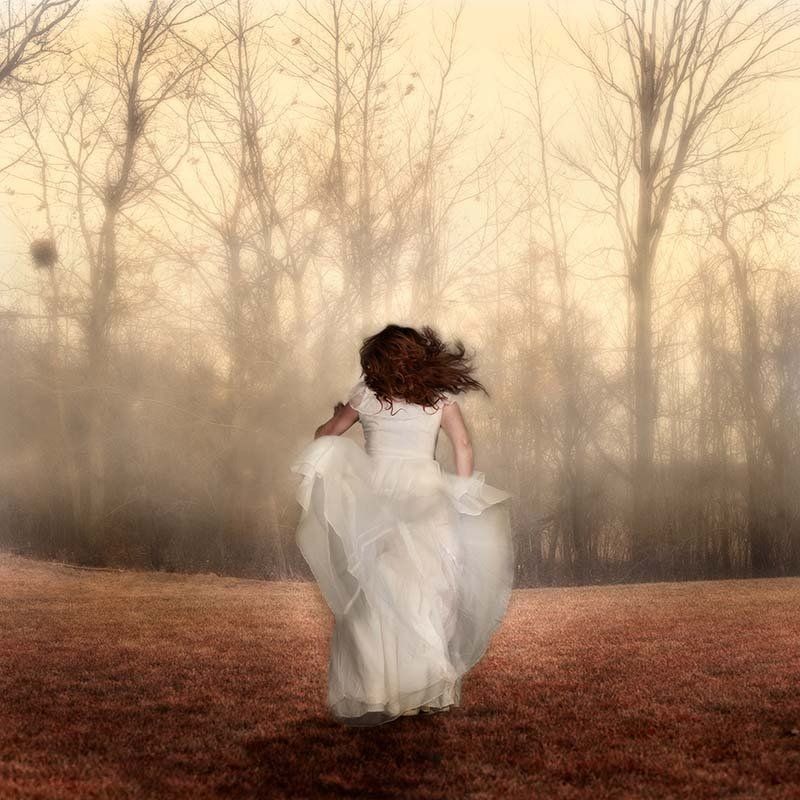 Person in a flowing white dress walking through a foggy autumn forest
