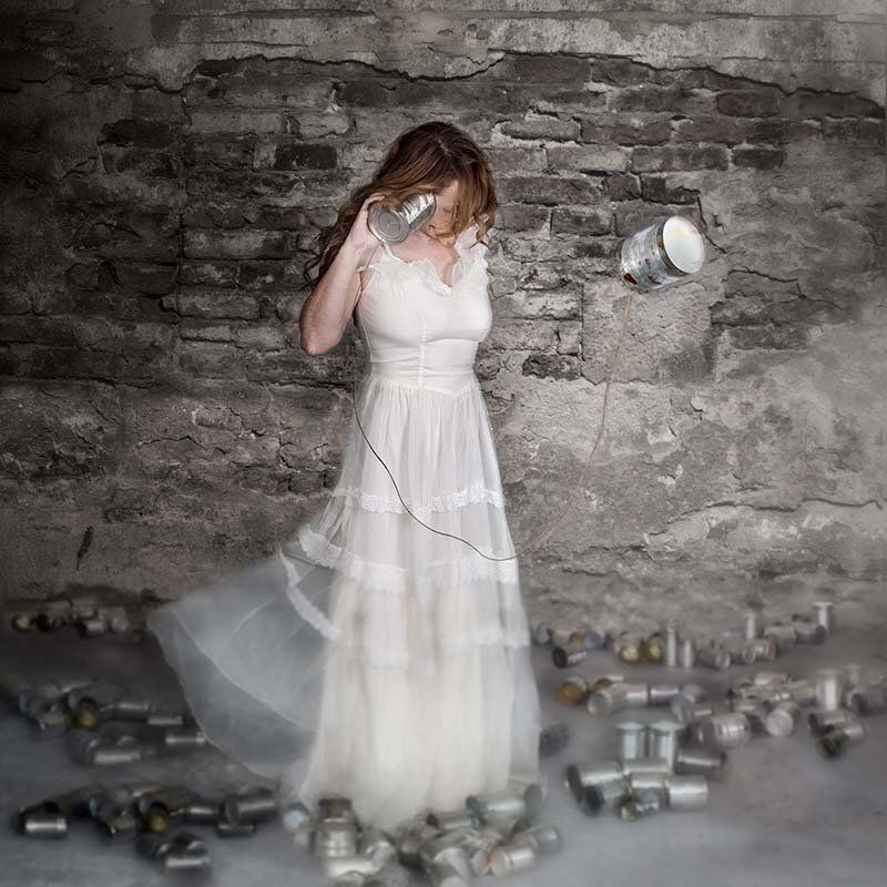 Woman in a white dress standing against a stone wall, surrounded by scattered metal cans.