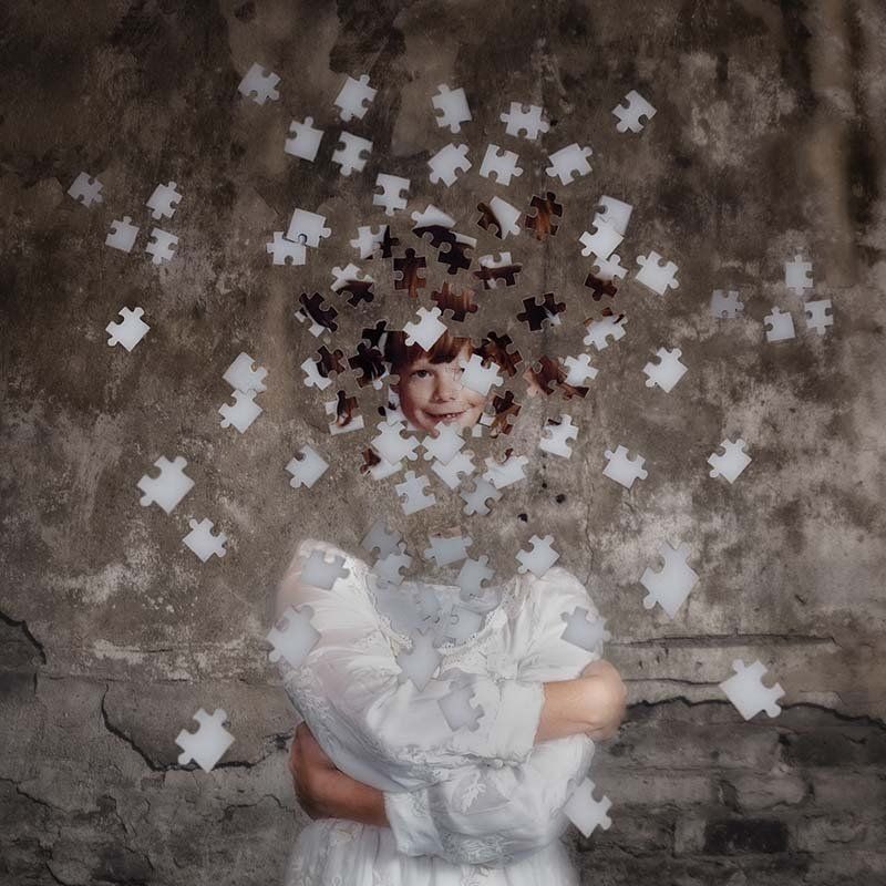 Person in white seated against a textured wall, with puzzle pieces swirling around their face.