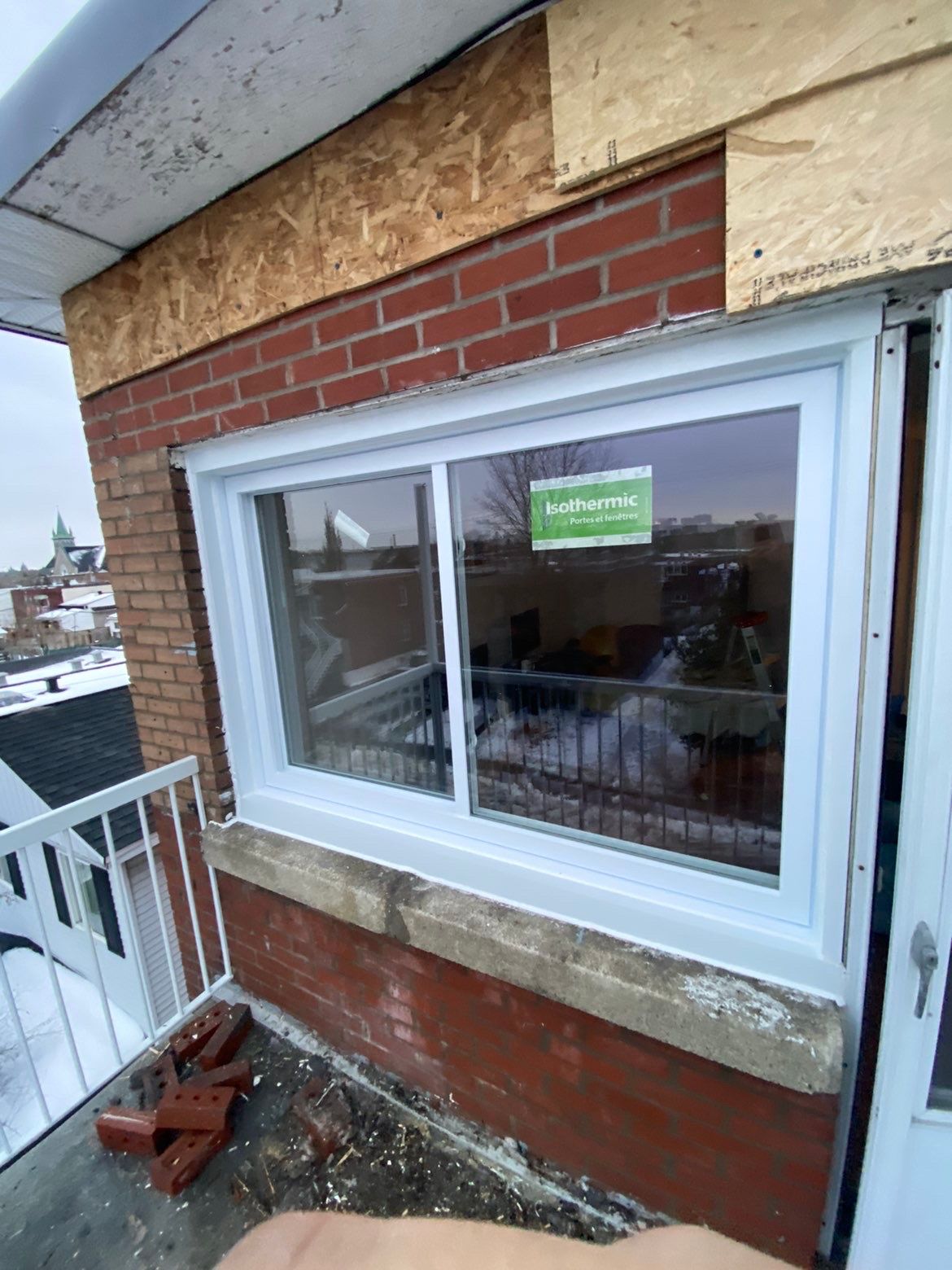 Fenêtre coulissante à cadre blanc installée sur un bâtiment en briques avec un petit balcon.