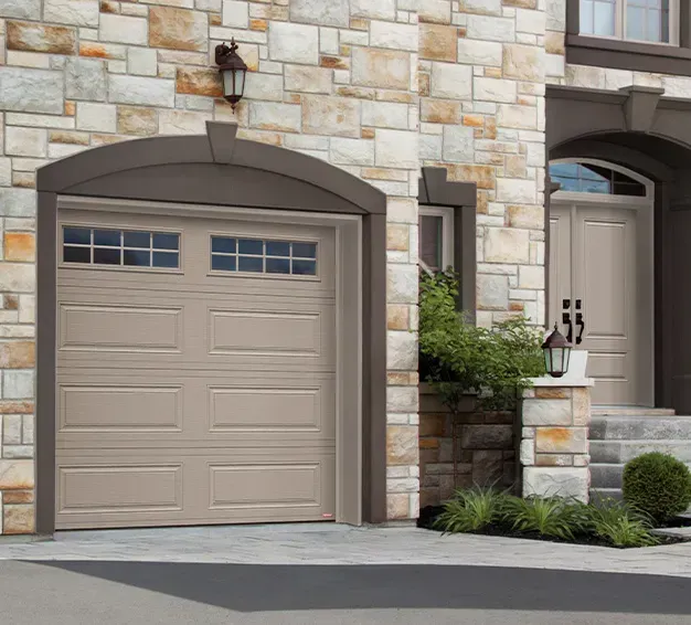 Porte de garage beige avec fenêtres sur une maison en pierre. Porte d'entrée visible à droite.
