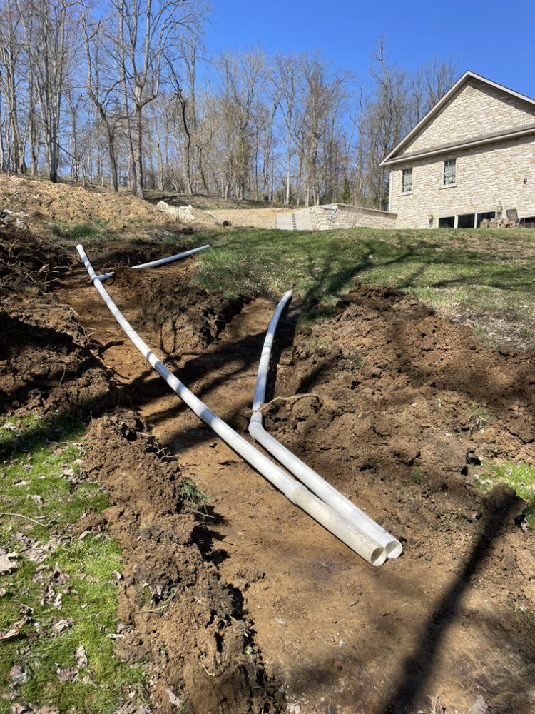 A couple of pipes are laying in the dirt in front of a house.