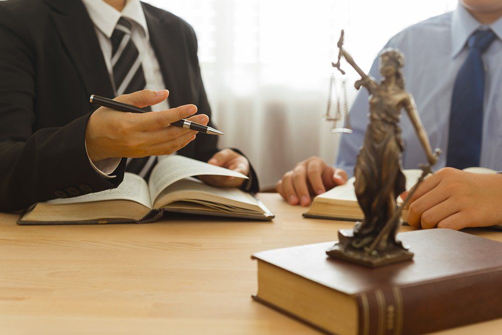 Two lawyers consulting, one pointing at a book, with the Statue of Justice on a table.