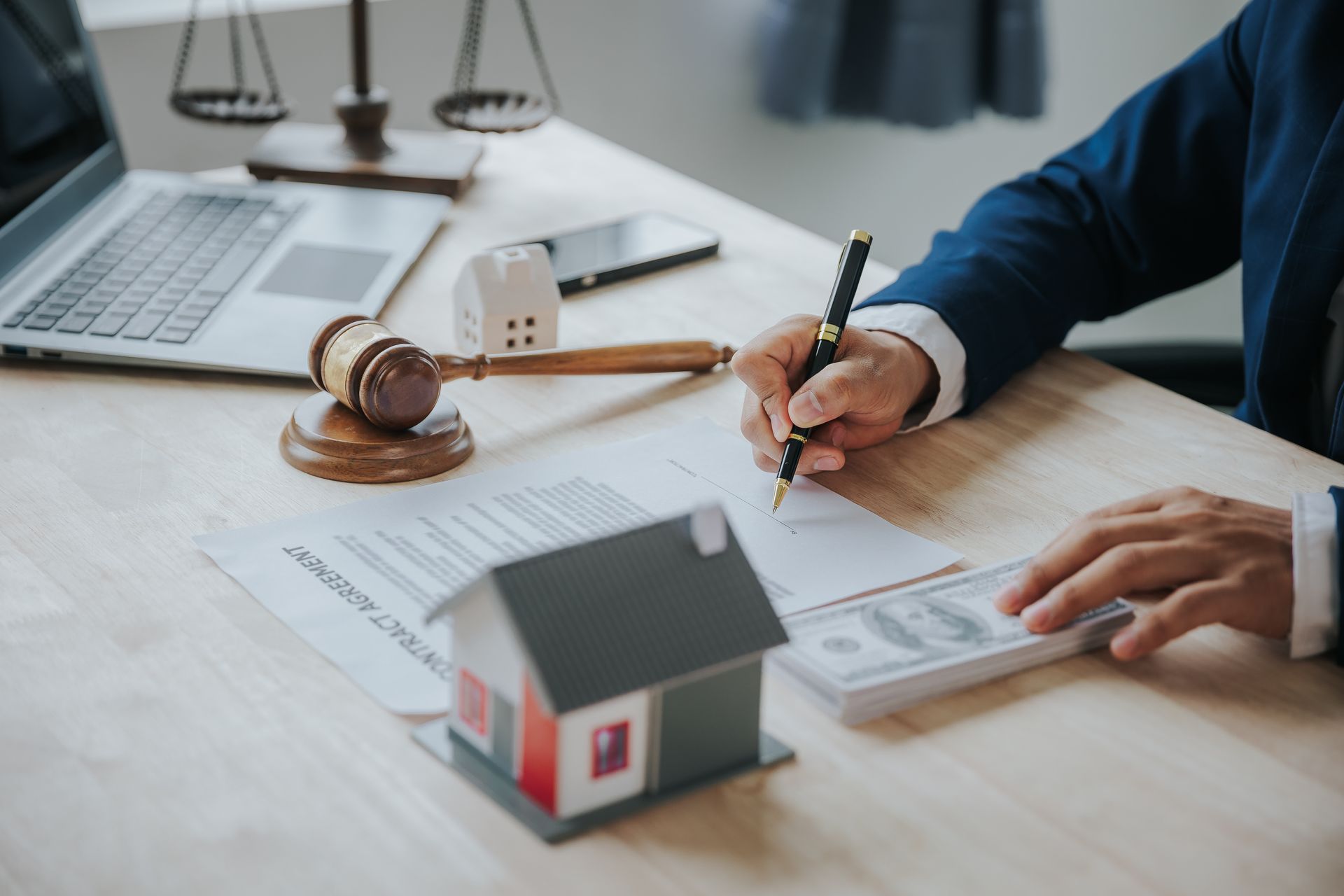 Attorney signing a real estate contract beside a gavel, model house, and cash