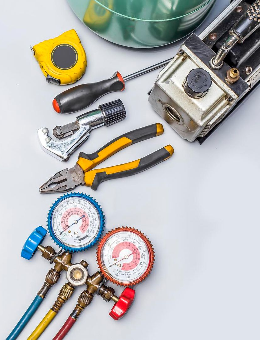 Assorted HVAC tools, gauges, pliers, wrench, tape measure, and equipment on a light background