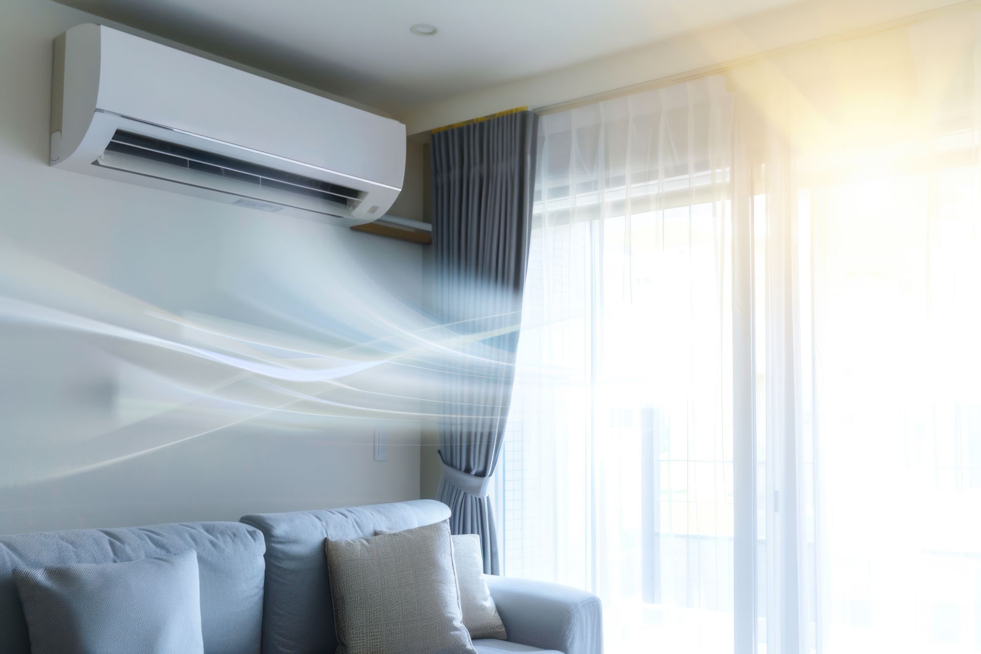 Living room with wall-mounted air conditioner blowing cool air toward a sofa and bright window curtains