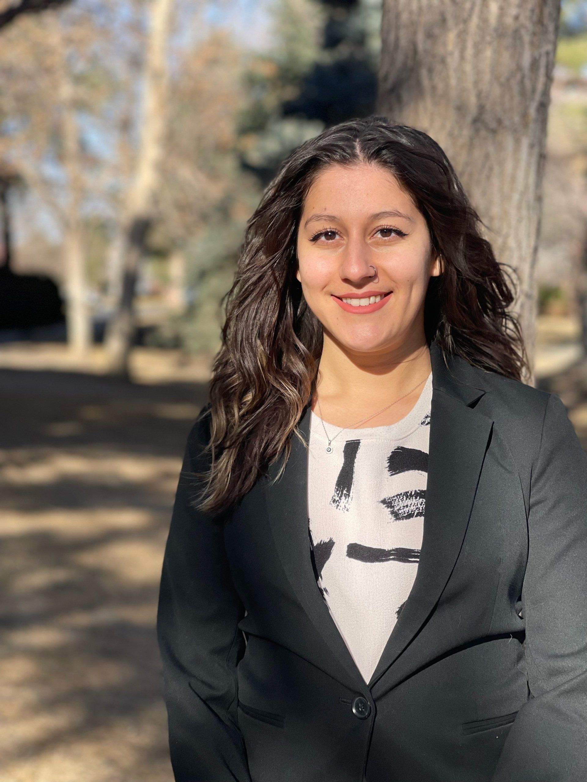 A woman in a suit is standing in front of a tree.