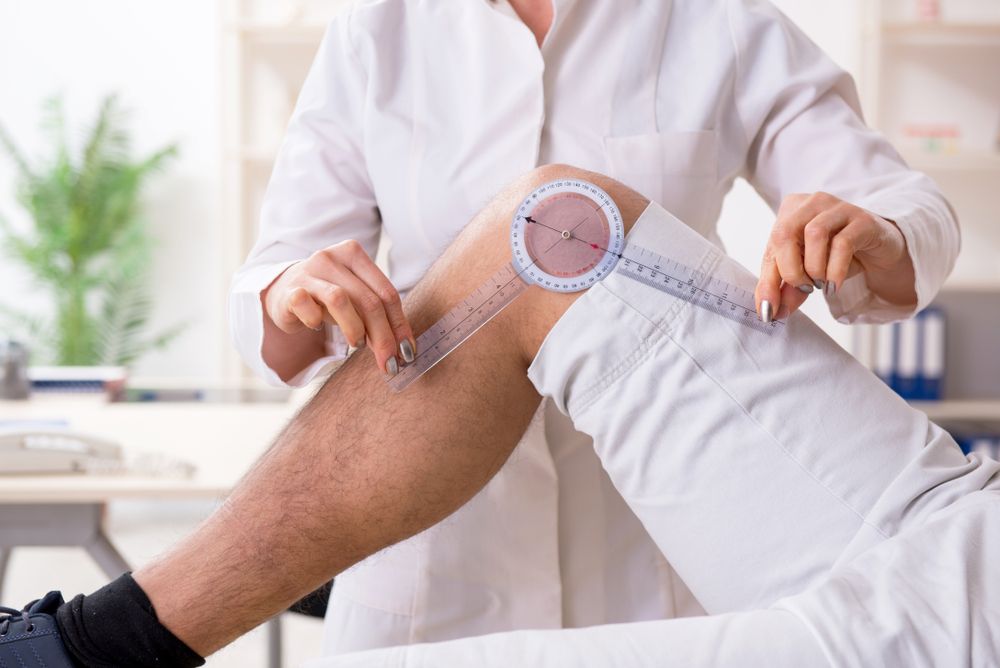 Doctor measuring a patient’s knee with a tape measure in a bright clinic