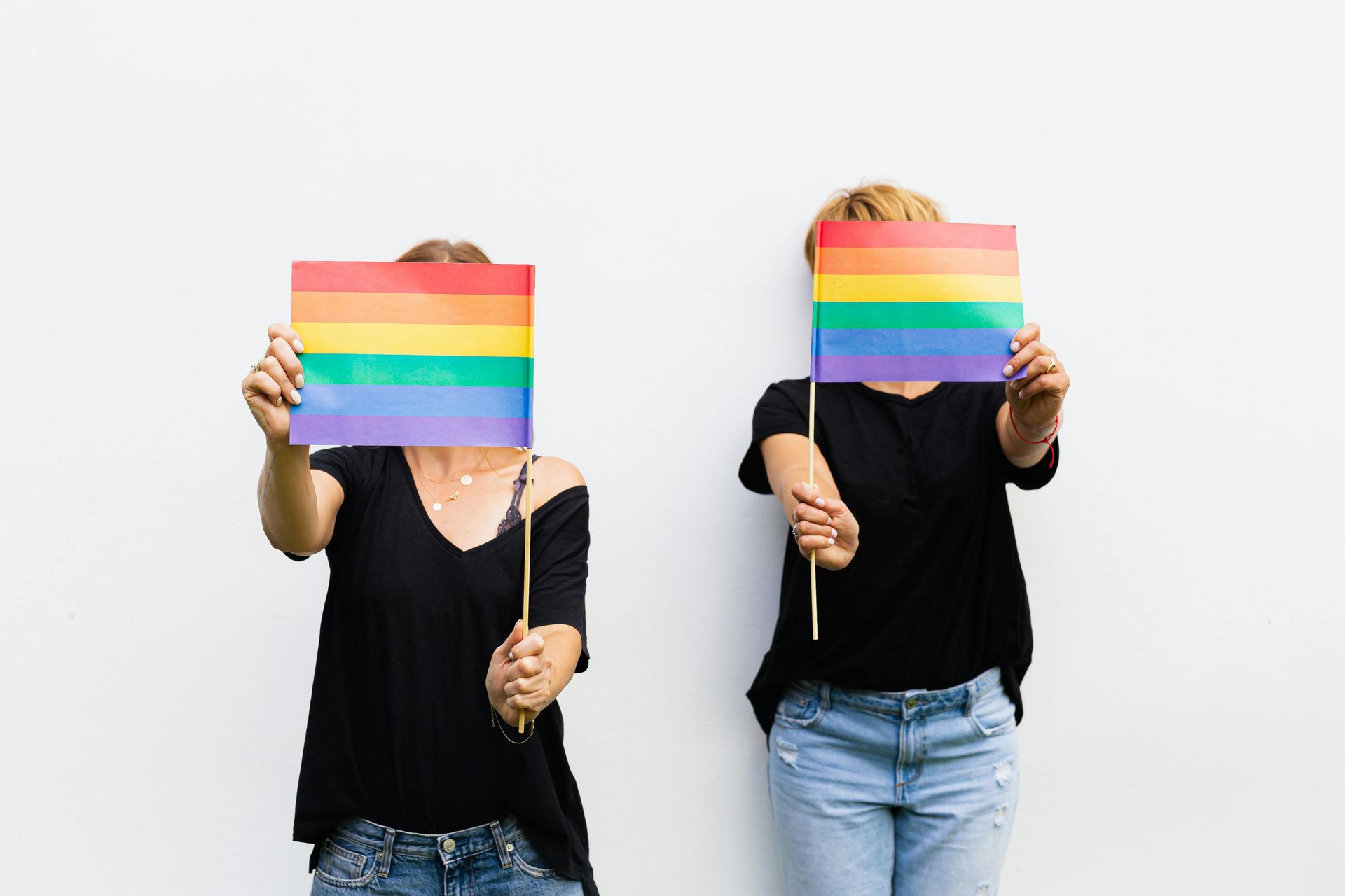 Two people holding rainbow pride flags over their faces against a white background