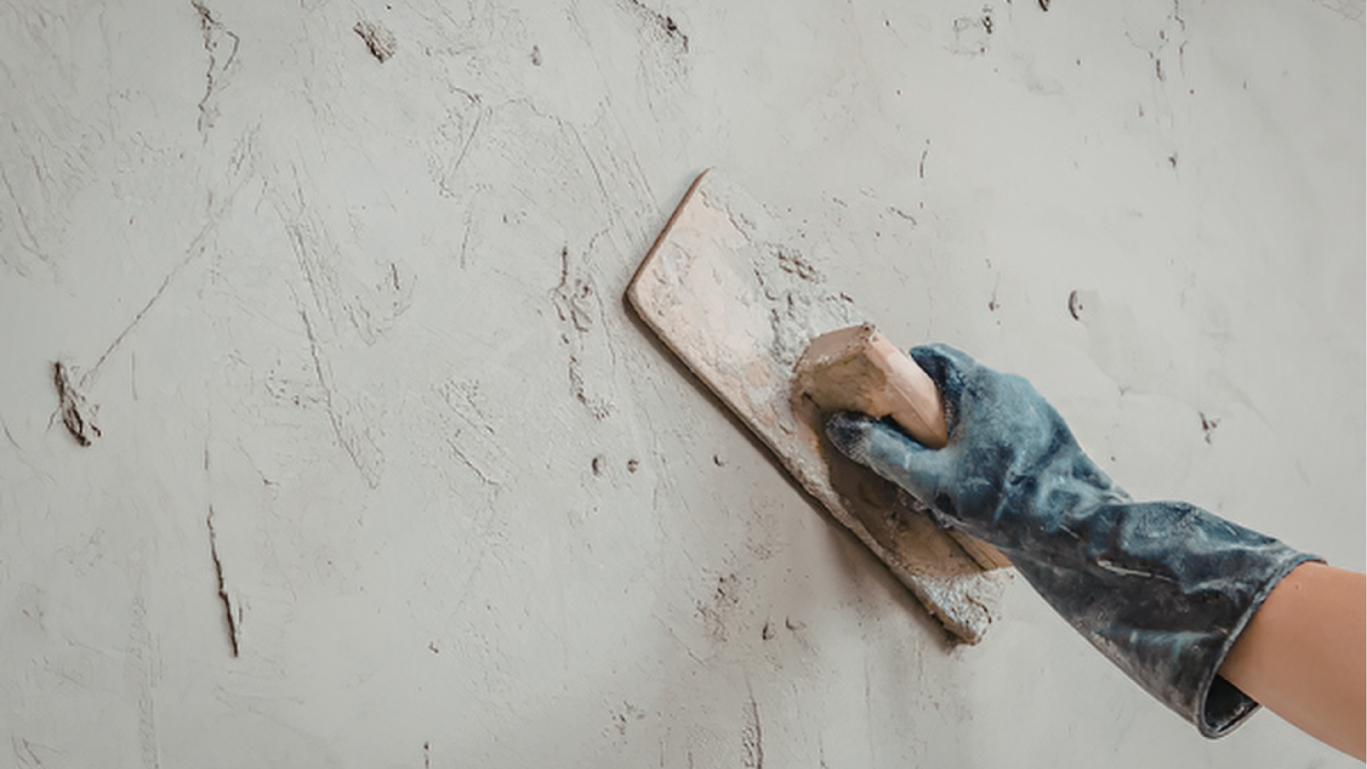 Hand in a blue glove smoothing plaster on a white wall with a trowel