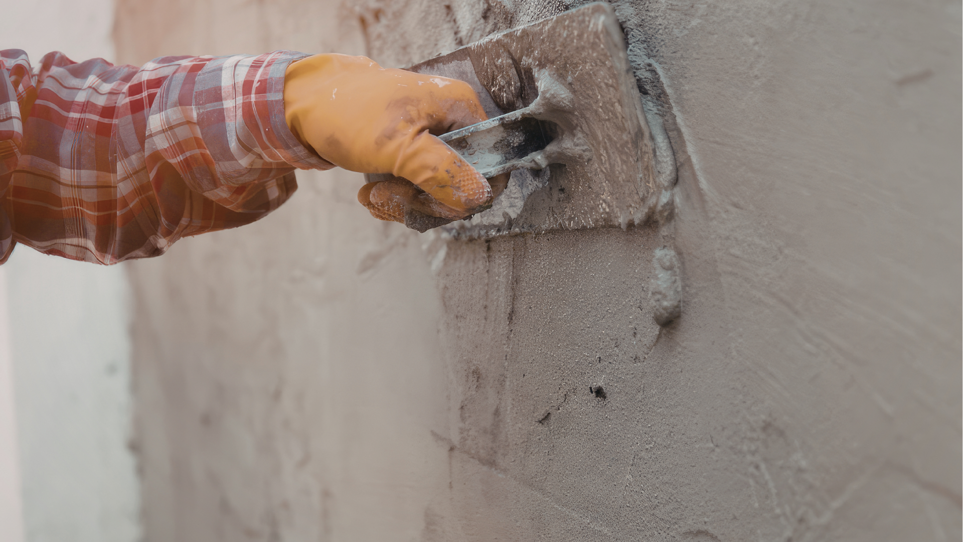 Gloved hand using a trowel to apply gray plaster to a wall