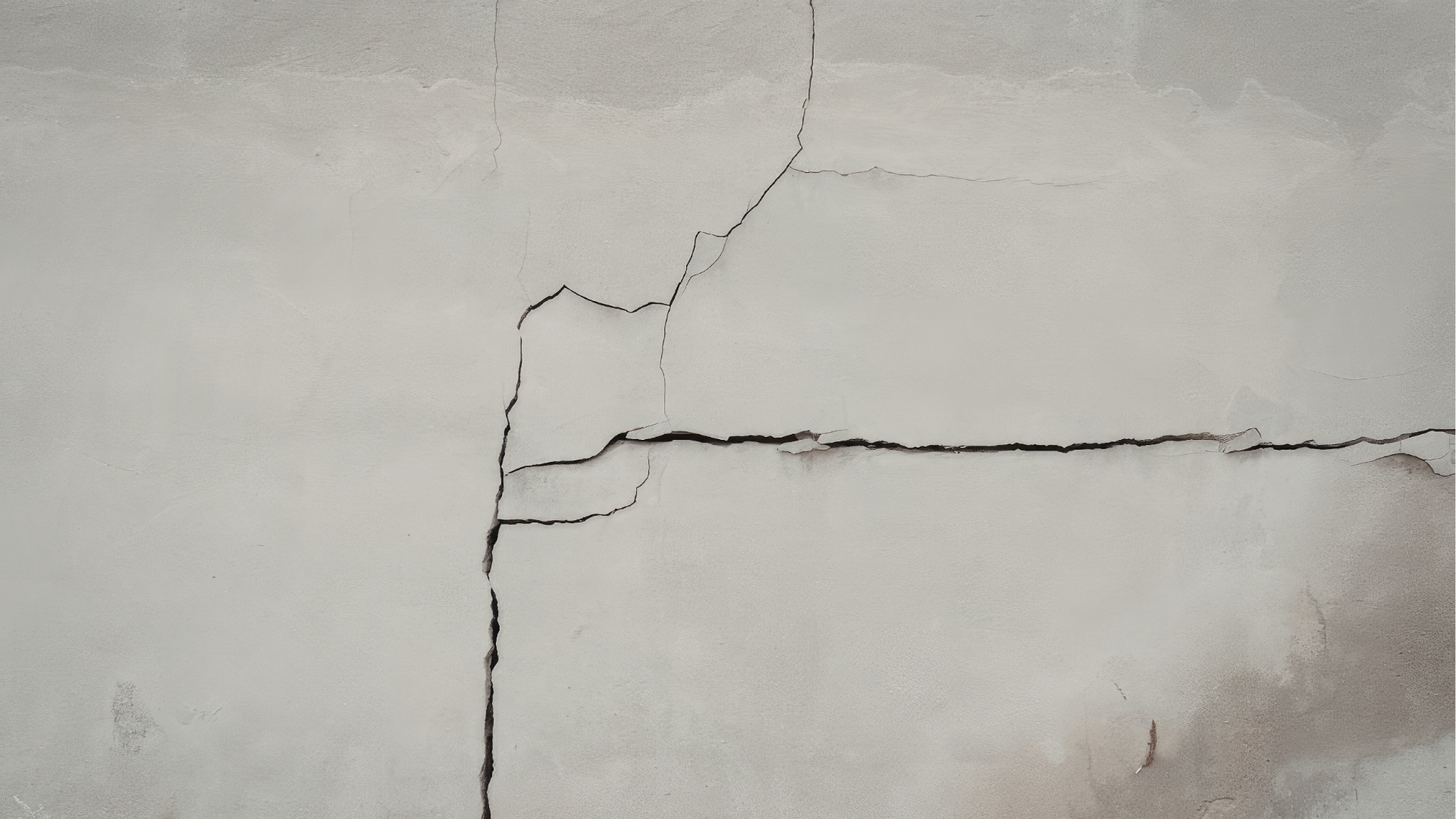 Close-up of a cracked white wall with a vertical and horizontal crack forming a corner