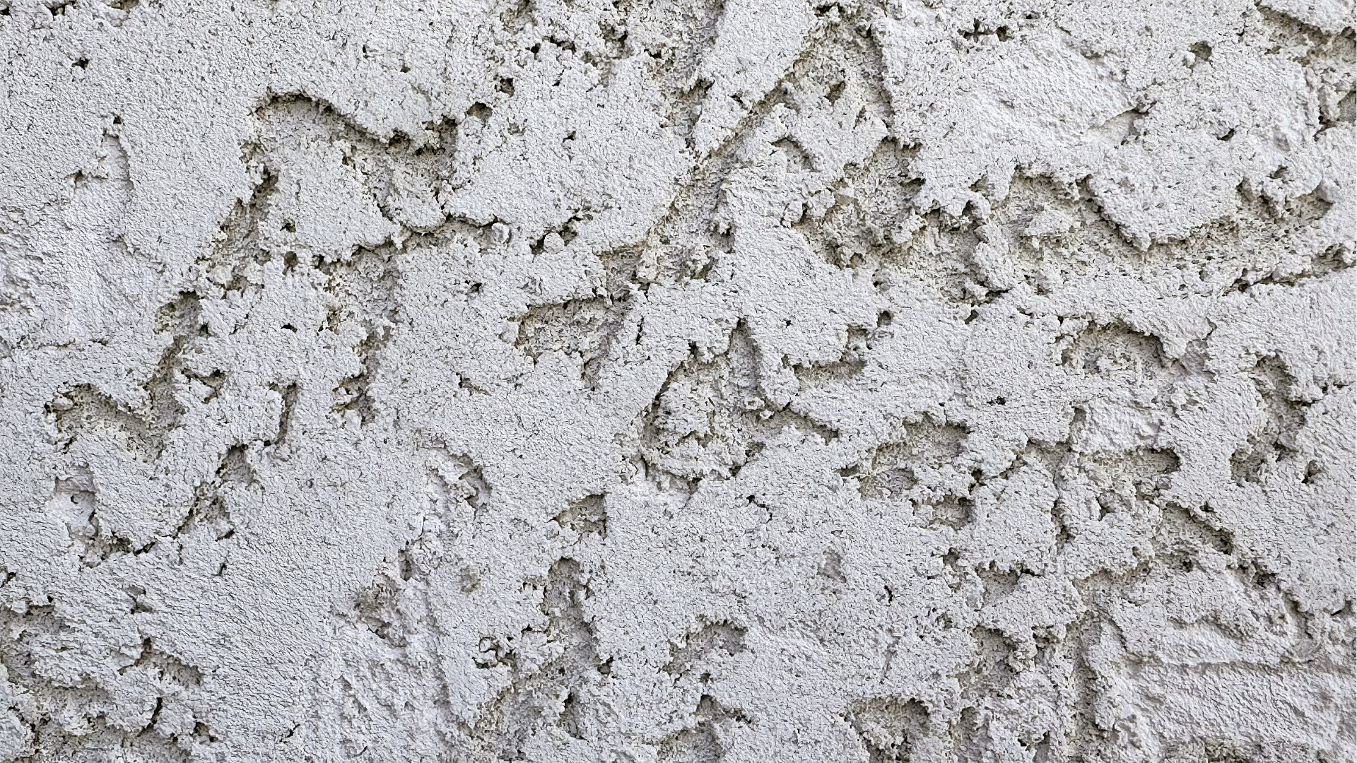Close-up of a textured gray and beige concrete or stucco surface with peeling patches