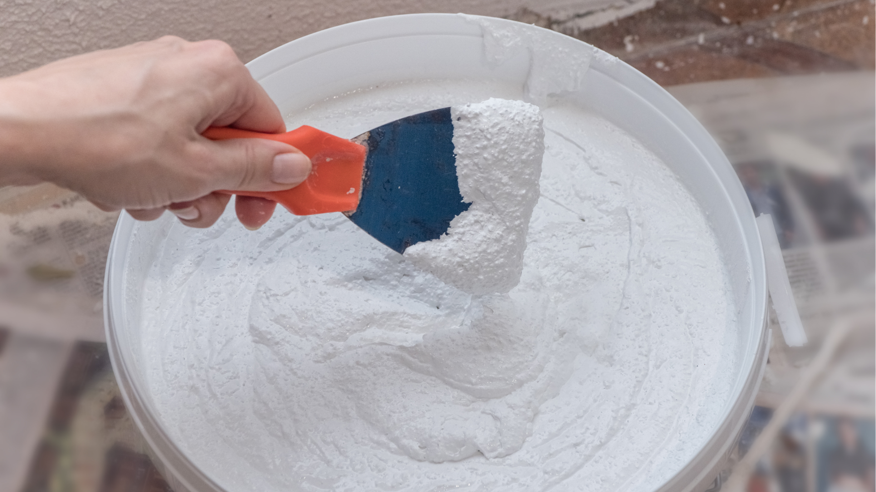 Hand scooping white powder from a bucket with an orange scoop