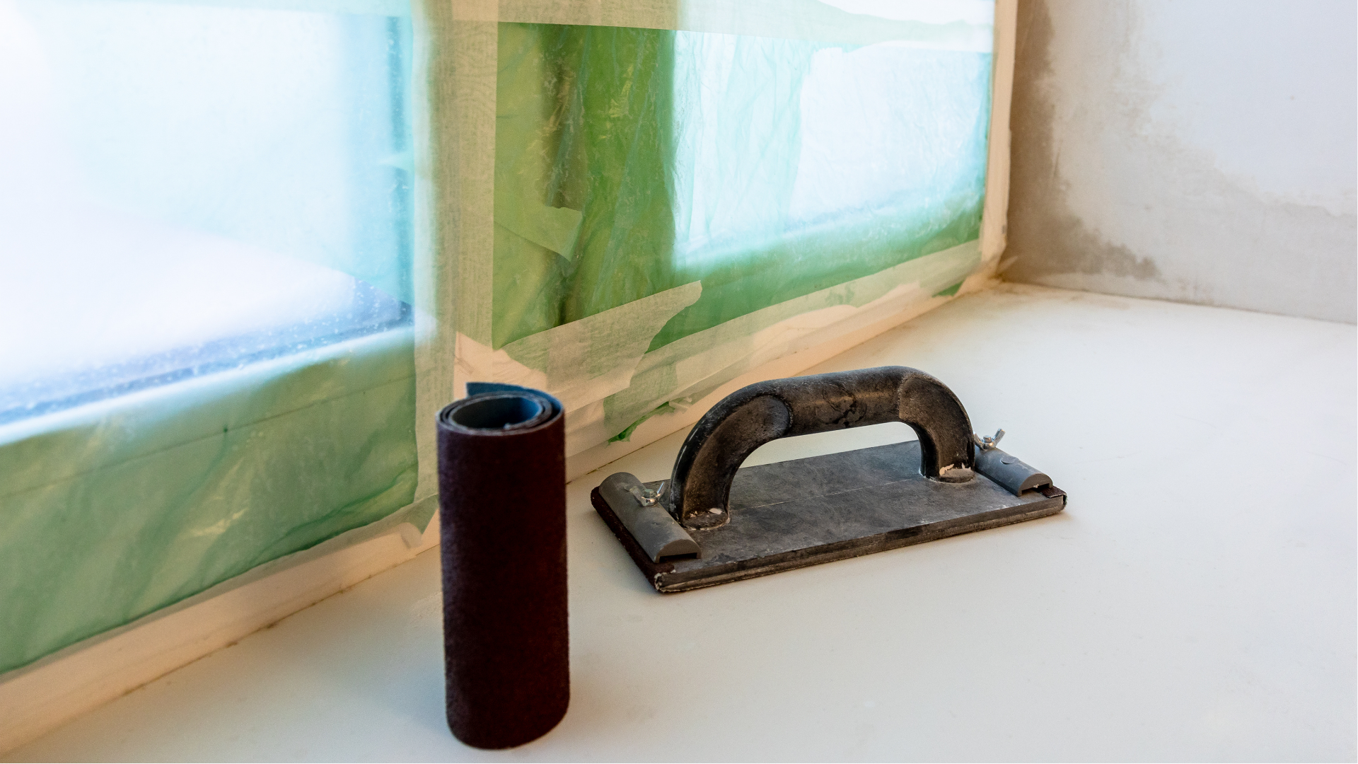Construction hand tool on a white windowsill beside taped-covered windows and a black tumbler.