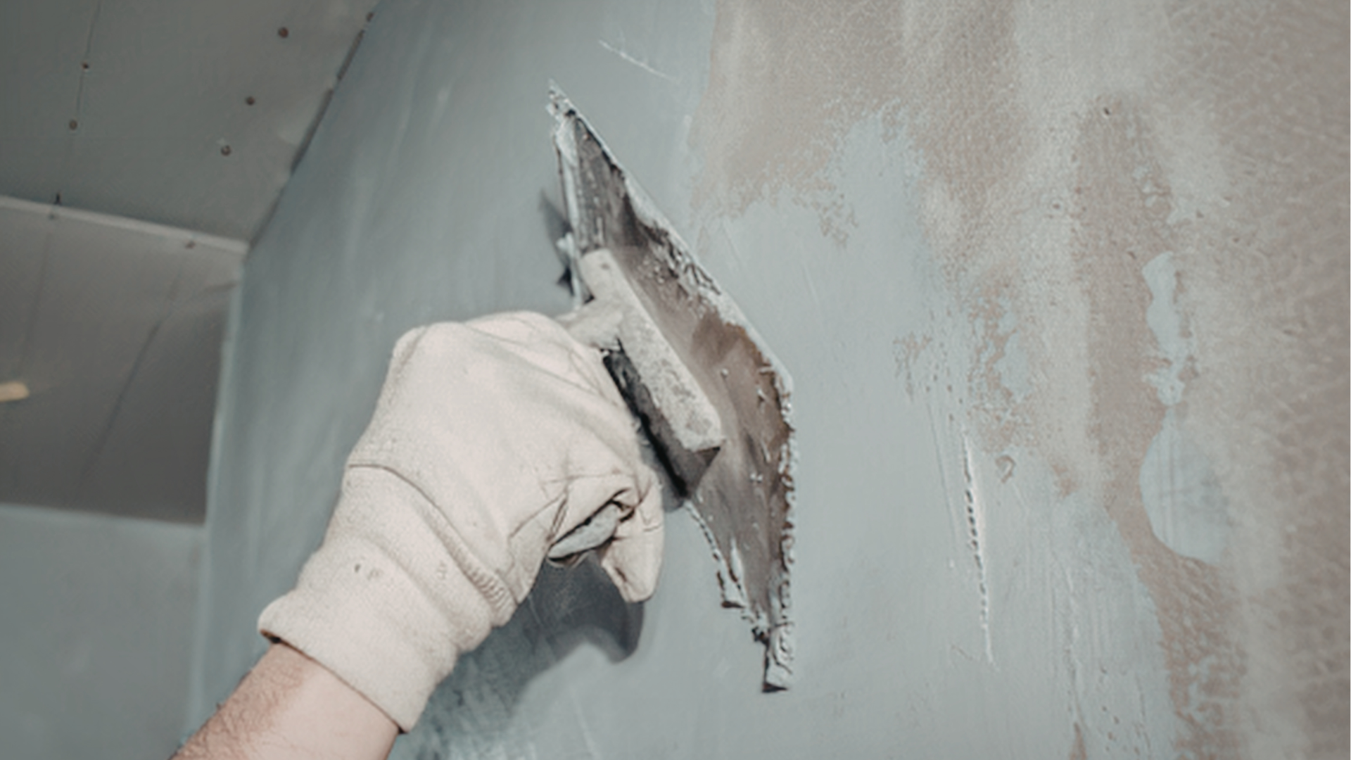 Gloved hand smoothing plaster on a damaged wall with a trowel during repair work