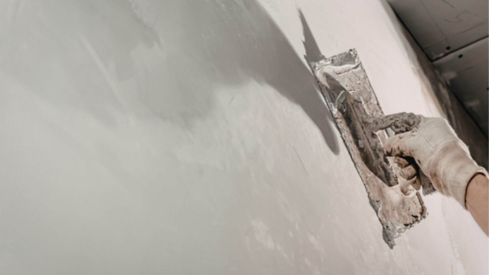 Hand in a glove smoothing gray plaster on a wall with a trowel