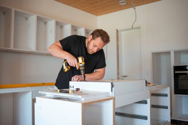 Man using a drill to assemble white kitchen cabinets in a bright room