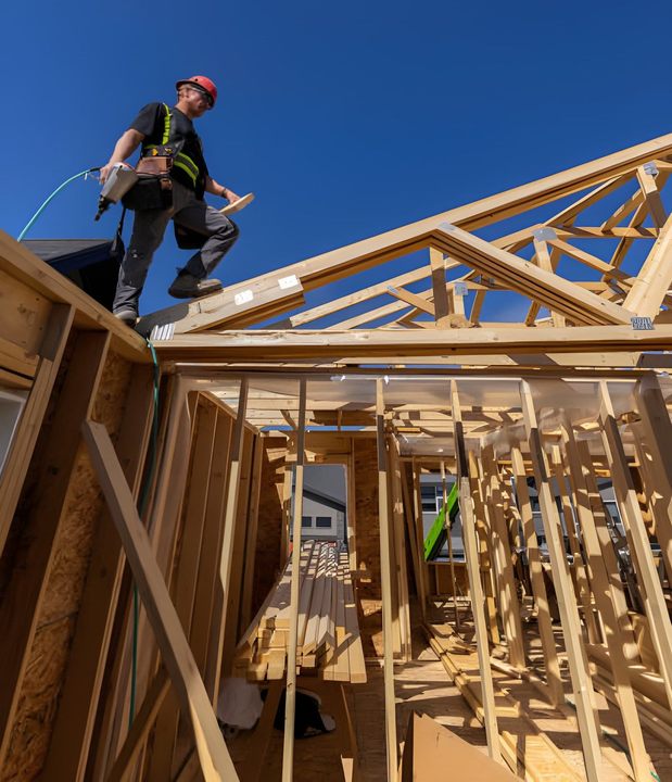 Construction worker on roof framing a house under a clear blue sky