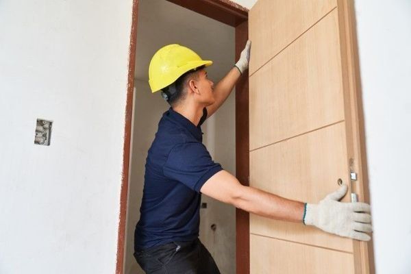Worker in a yellow hard hat installing a wooden door in a doorway