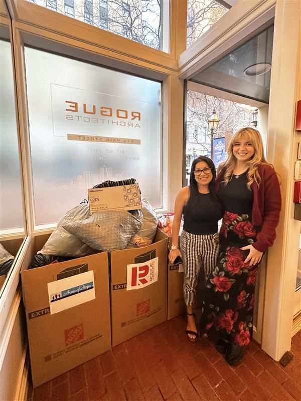 Two women are standing next to each other in a room filled with cardboard boxes.