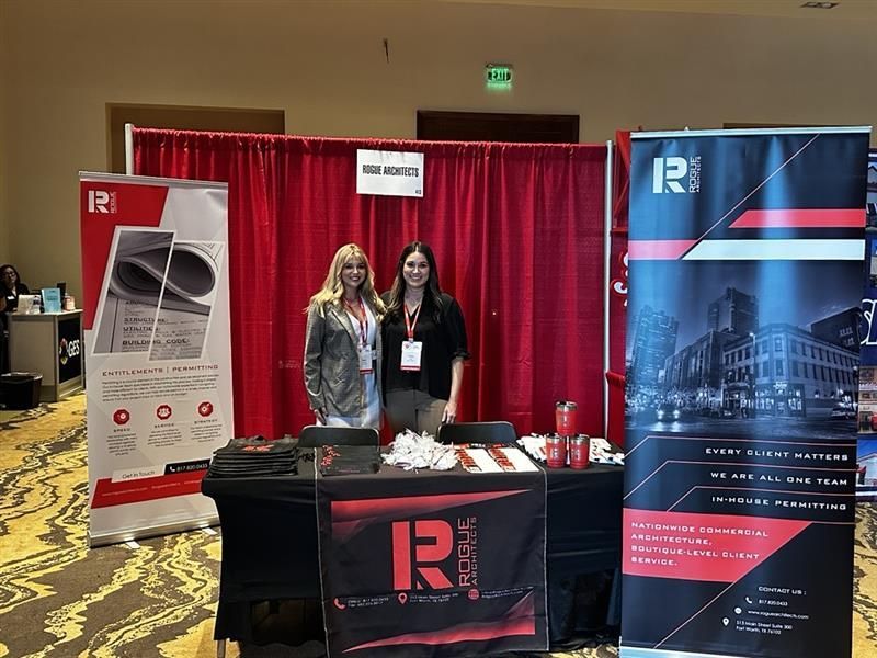 Two women are standing in front of a table at a convention.