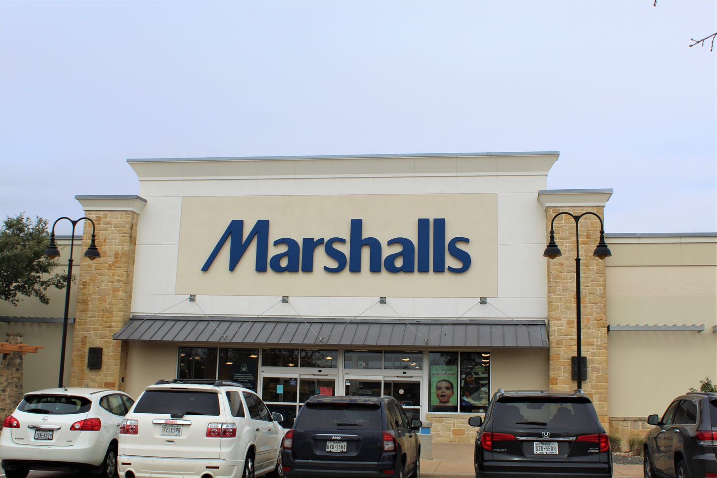 A row of cars are parked in front of a marshalls store.