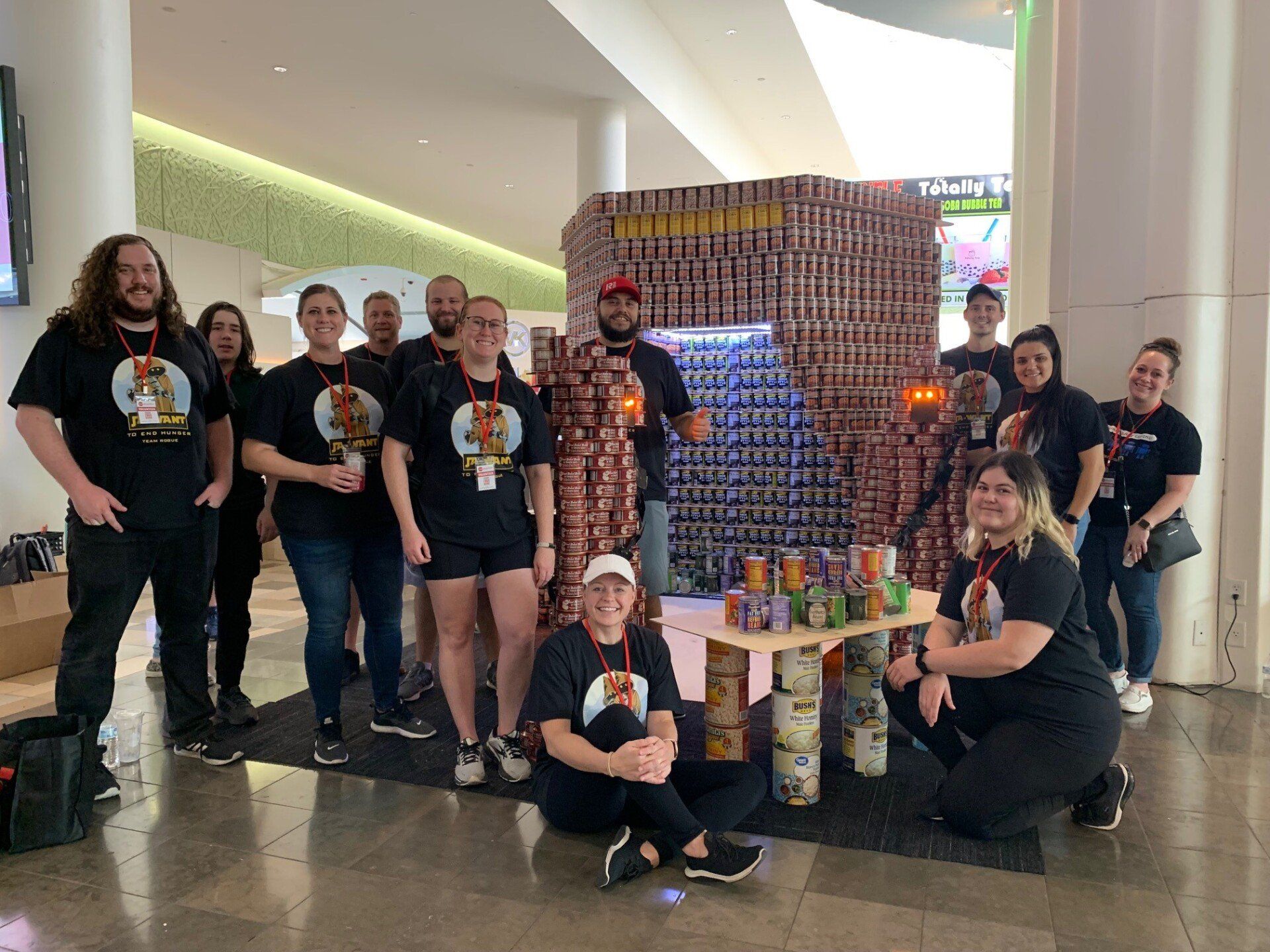 A group of people are posing for a picture in front of a wall made out of cans.