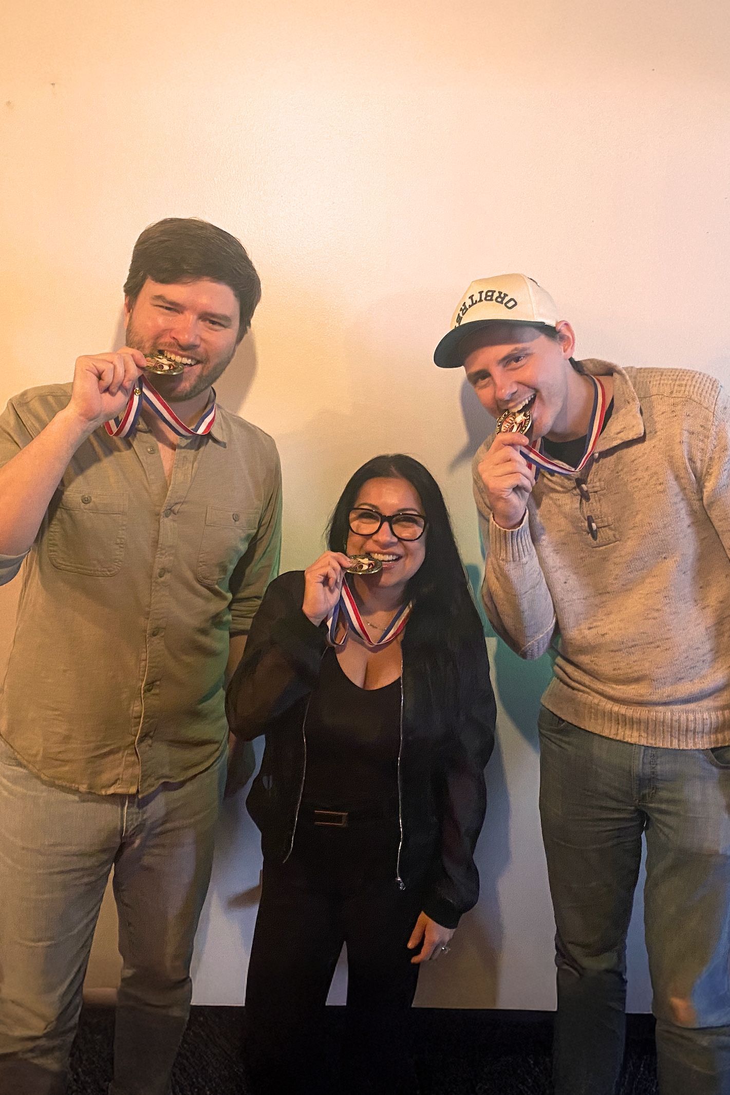 Three people posing indoors, smiling and holding medals for the Chili Cook Off