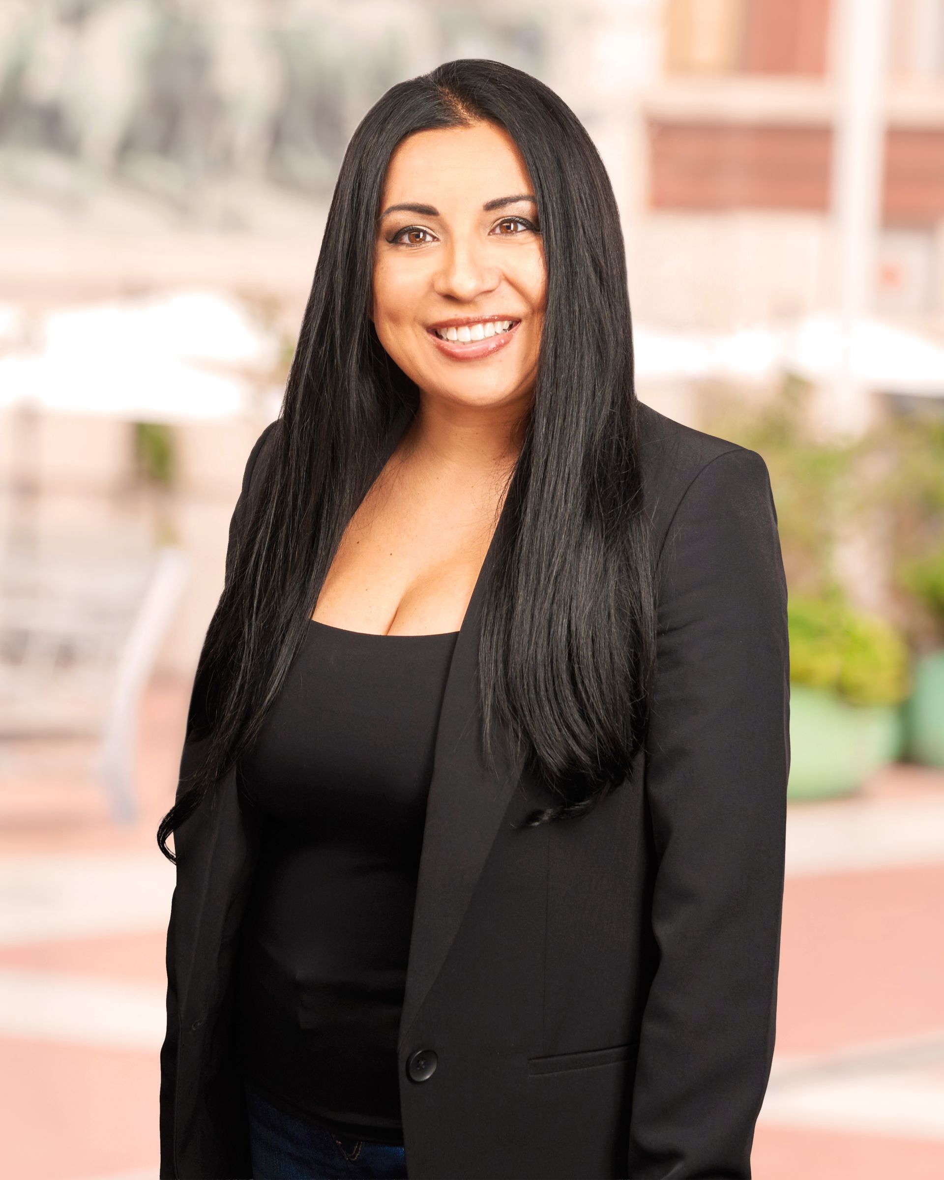 A woman with long black hair is wearing a black jacket and smiling.