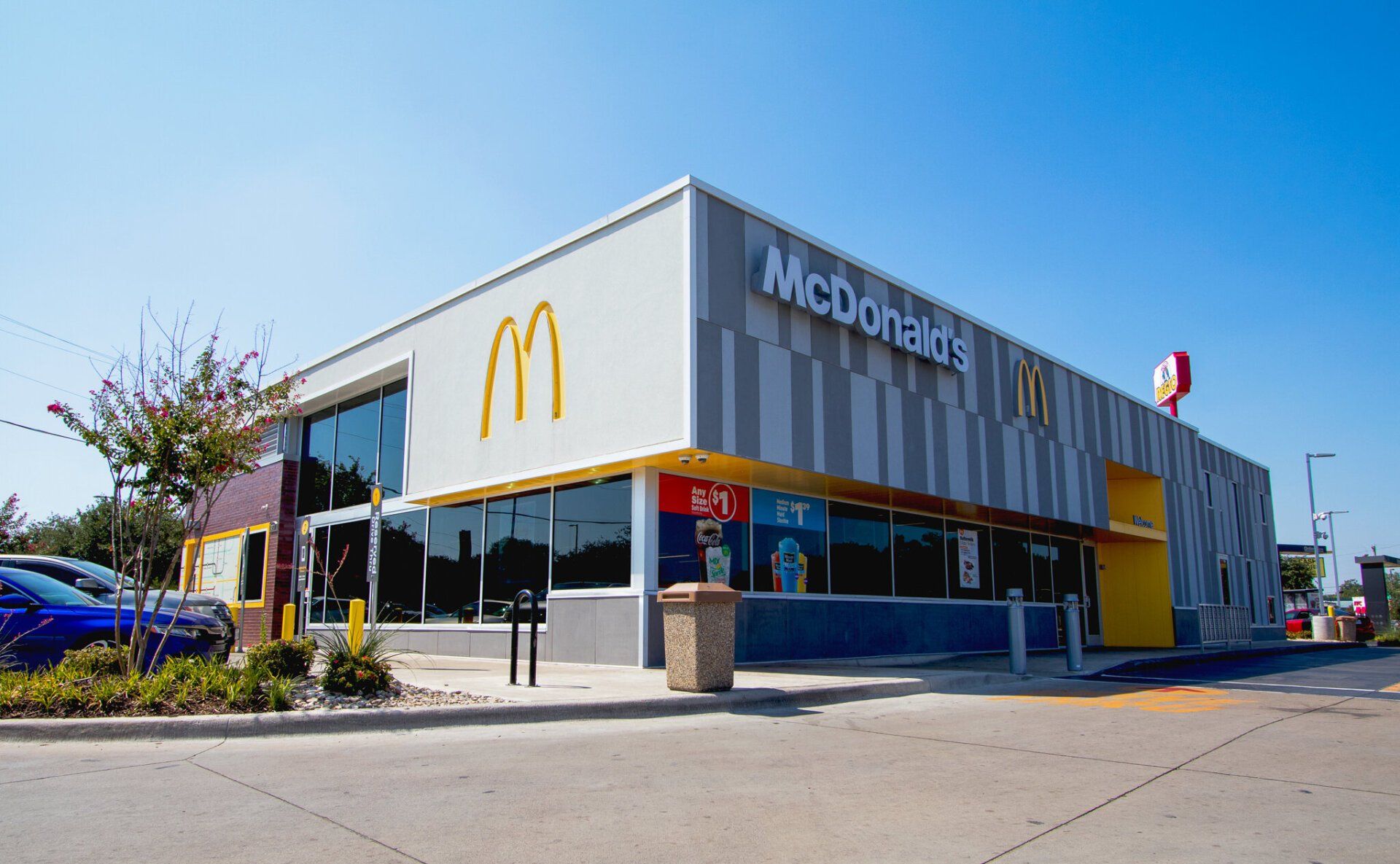The outside of a mcdonald 's restaurant with cars parked in front of it.
