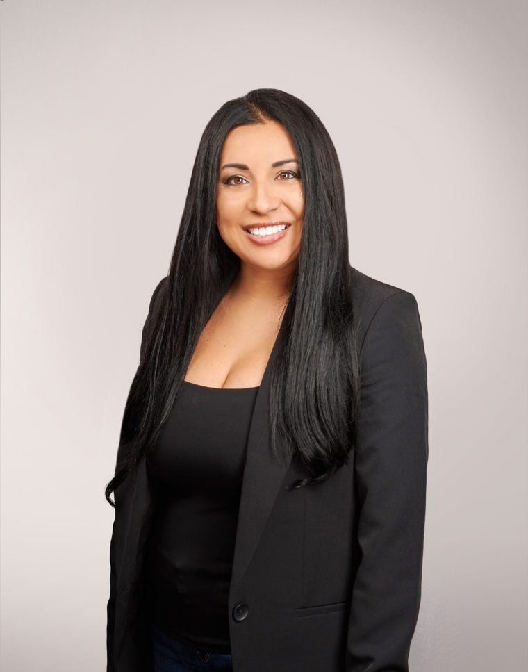 A woman with long black hair is wearing a black jacket and smiling.